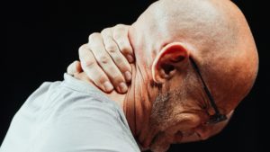 bald person holding their neck in pain