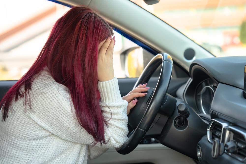 Woman behind the wheel of a car, holding her head: feeling unwell, accident.