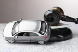 Motor vehicle accident law. Gavel, money and car model on grey background, closeup