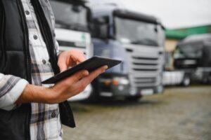 Man holding a digital tablet managing fleet operations and freight logistics, standing near a lineup of transport trucks