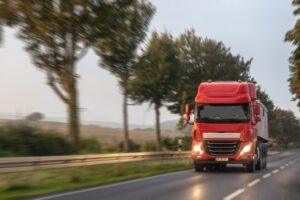 Red semi on rural highway with headlights. Morning delivery.