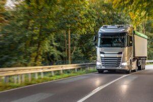 Large modern truck on winding road through green forest. Freight logistics.