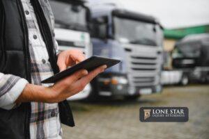 Man holding a digital tablet managing fleet operations and freight logistics, standing near a lineup of transport trucks